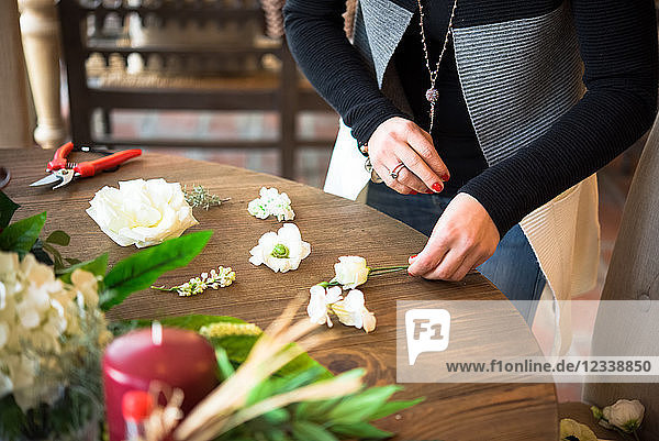 Frau arrangiert Blumenköpfe und Stiele auf Holztisch  Mittelteil