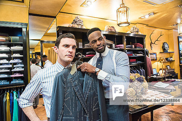Tailor holding bespoke suit jacket against customer in tailors shop