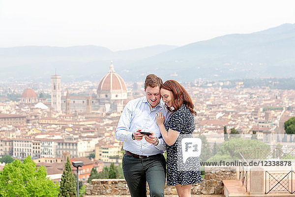 Junges Paar lächelt am Handy  Santa Maria del Fiore im Hintergrund  Florenz  Toskana  Italien