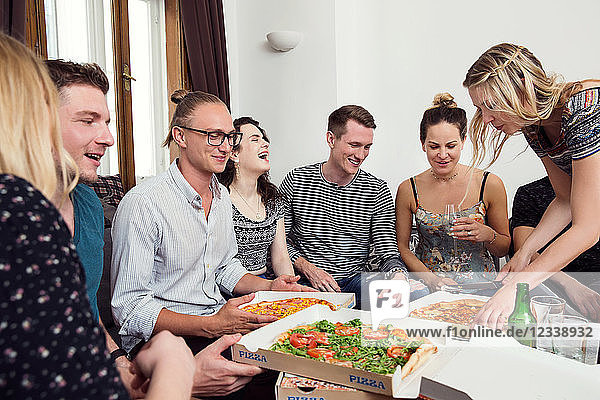 Group of friends chatting over drinks and pizza at home