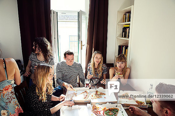 Eine Gruppe von Freunden unterhält sich bei Getränken und Pizza zu Hause