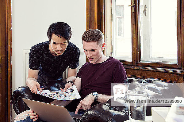 Zwei junge Männer mit Ausdrucken am Laptop