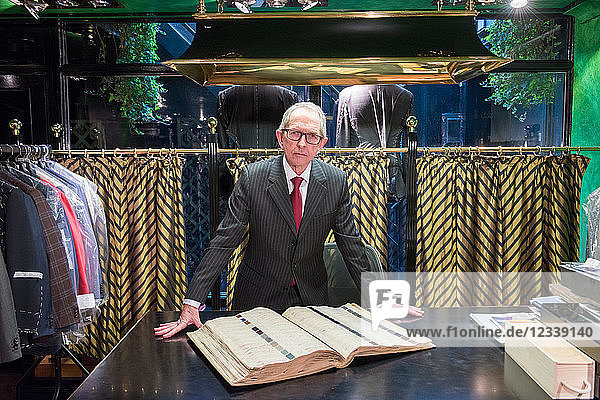 Senior tailor looking at handmade swatch book in traditional tailors shop  portrait