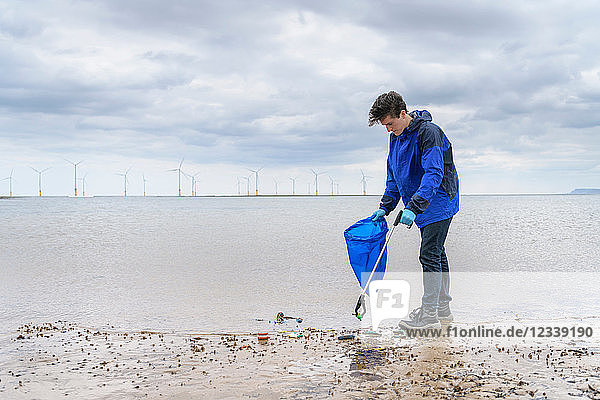 Man using litter picker to remove plastic pollution collected on beach, North East England, UK