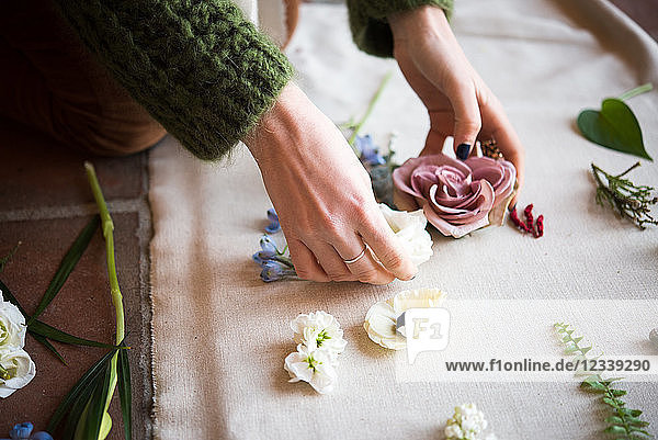 Frau arrangiert pastellfarbene Blumenköpfe und Blattstiele auf Textil  Detail der Hände
