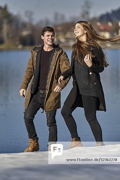 Tegernsee  Germany  playful couple walking next to lake  candid expression  sunny weather  winter