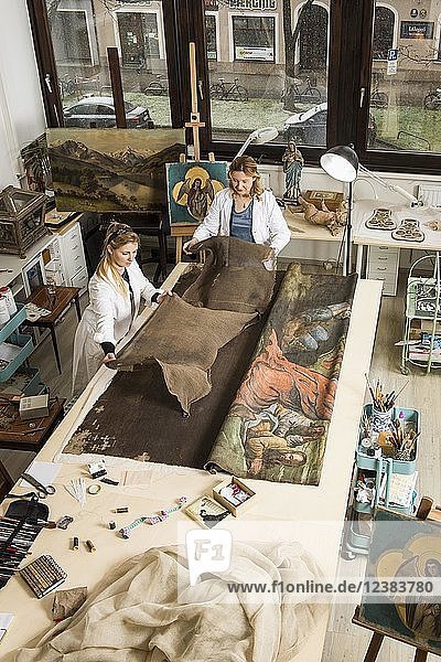 Restaurierungsatelier  Restauratoren  Frauen legen ein fertiges Stück Leinen für Stützgewebe auf einen Arbeitstisch mit geliehenem Schal im Atelier  München  Bayern  Deutschland.
