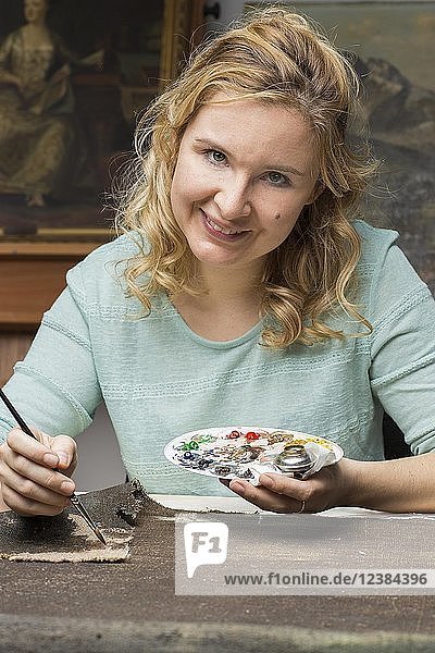 Restaurierungsatelier  Restauratorin  Frau patiniert das eingewebte Leinenstück mit Pinsel und Farbe  München  Bayern  Deutschland  Europa
