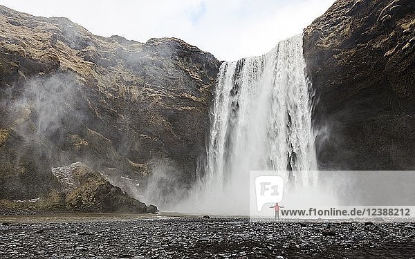 Hiker with red jacket in front of a high waterfall Skogafoss  Skogar  South Iceland  Iceland  Europe