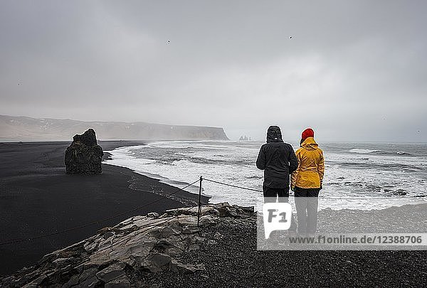 Two tourists overlooking a black sandy beach  bad weather  Reynisfjara Beach  South Iceland  Iceland  Europe