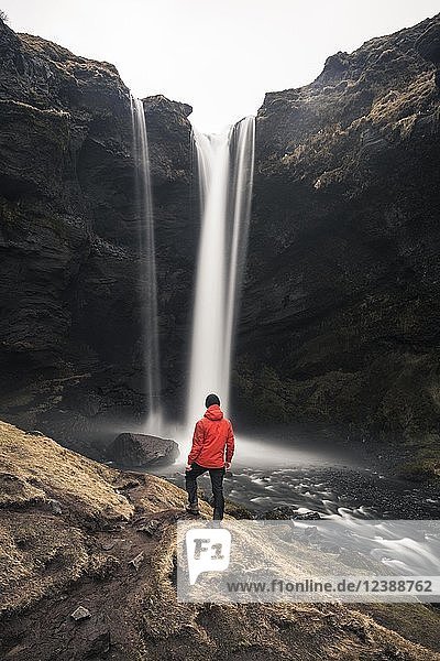 Man in red jacket in front of Kvernufoss waterfall in a gorge  dramatic atmosphere  time exposure  near Skógafoss  Southurland  Iceland  Europe