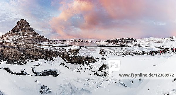 Kirkjufell Berg  Kirkjufellfoss Wasserfall vor gefroren  bewölkter Himmel mit Sonnenuntergang  Grundarfjördur Fjord  Westisland  Island  Europa