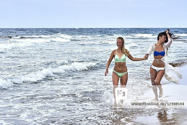 Two young women running at beach in bikini  holding hands. Malia  Crete  Greece.