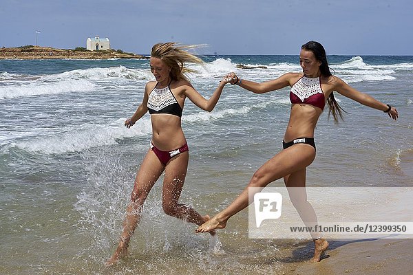 Two women running at beach in sea water  wearing bikini. Having fun. Holiday location Greece  Crete  Malia