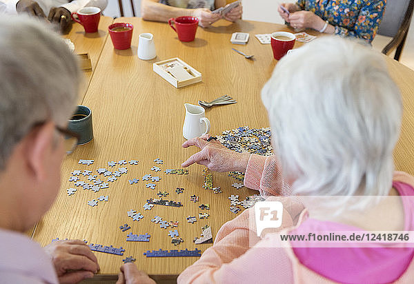 Senior friends assembling jigsaw puzzle at table in community center