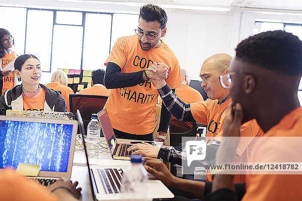 Hackers handshaking  celebrating and coding for charity at hackathon
