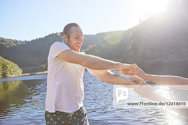 Playful couple holding hands at sunny summer lake