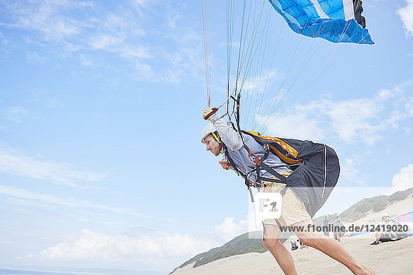 Male paraglider running with parachute on beach