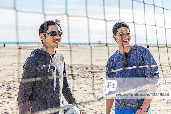 Smiling men playing beach volleyball on sunny beach