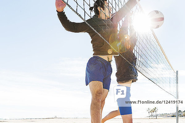 Men playing beach volleyball on sunny beach