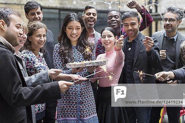 Friends with sparklers celebrating with woman holding birthday cake