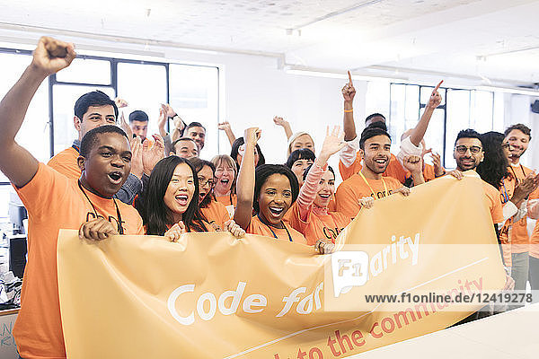 Portrait enthusiastic hackers cheering with banner  coding for charity at hackathon
