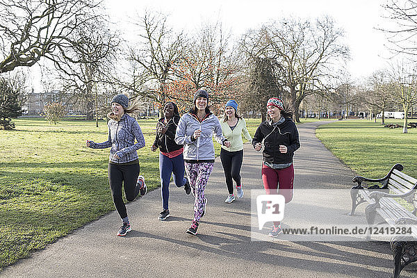 Smiling female runners running in sunny park