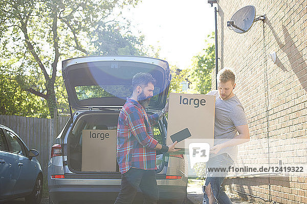 Male gay couple unloading moving boxes from car