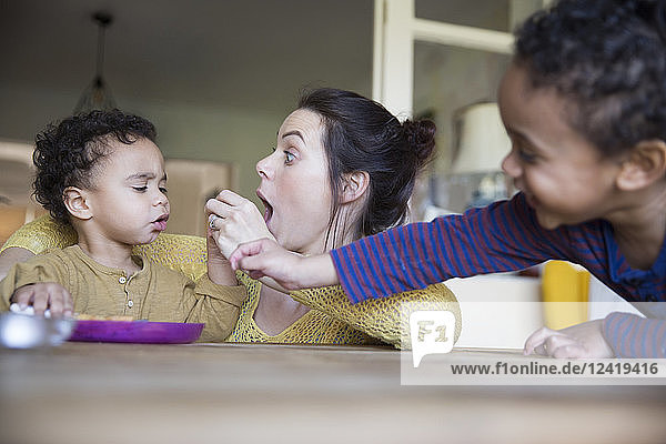 Verspielte Mutter füttert ihren kleinen Sohn am Tisch