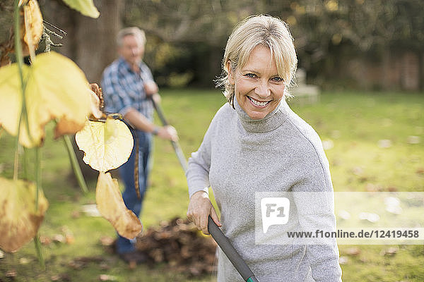 Porträt lächelnd  zuversichtlich  reife Frau harken Blätter im Herbst Hinterhof