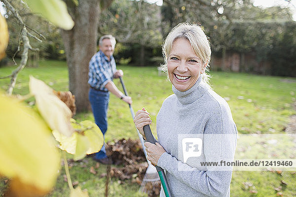 Portrait smiling confident mature woman raking autumn leaves in backyard
