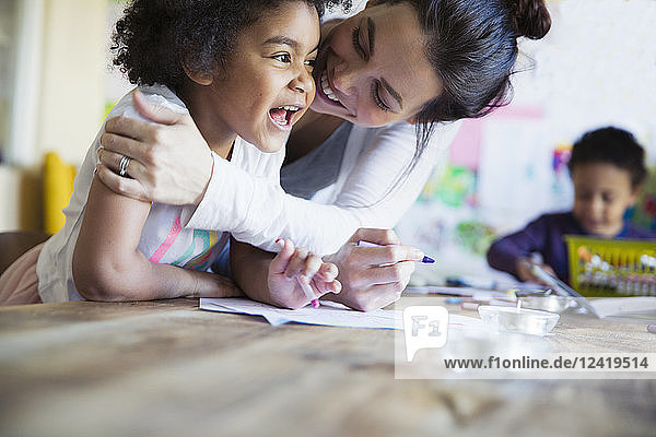 Affectionate  happy mother hugging toddler daughter coloring at table