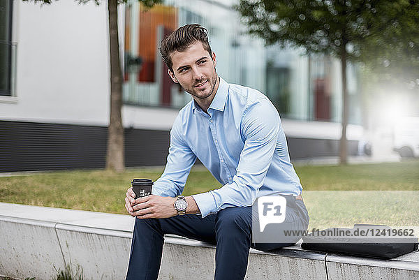Smiling businessman sitting outdoors with takeaway coffee