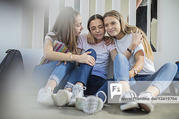 Smiling teenage girls sitting on floor in school hugging