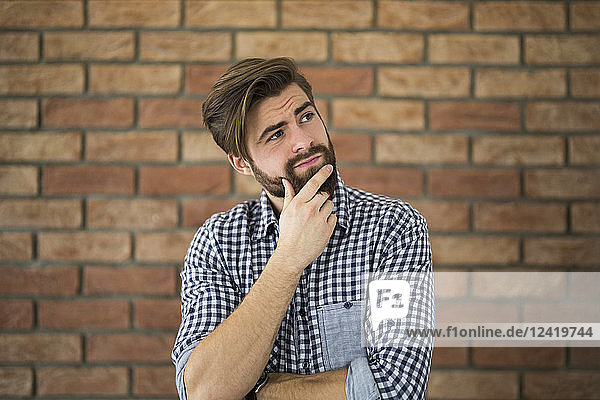 Portrait of pensive young man in front of brick wall