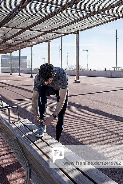 Sportive man lacing his shoes on a bench under roofing