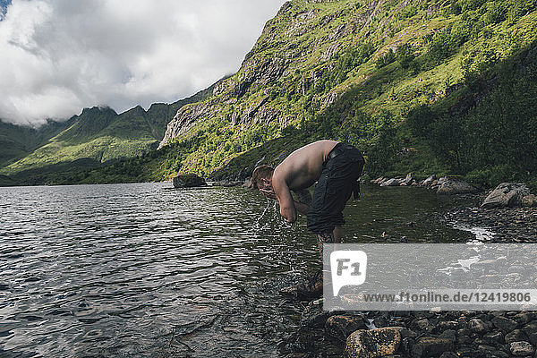 Norway  Lofoten  Moskenesoy  Young man washing his face in Agvatnet lake
