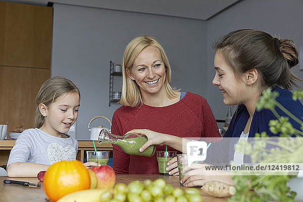 Mother with daughters sitting in kitchen  drinking homemade fruit smoothie