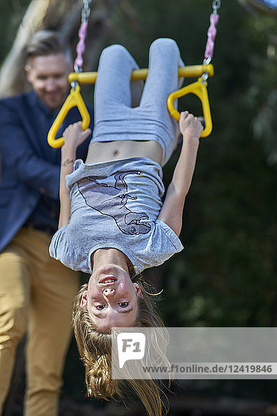 Girl hanging on trapeze with father in background