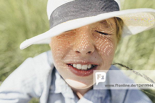 Boy with closed eyes wearing a hat sitting in field