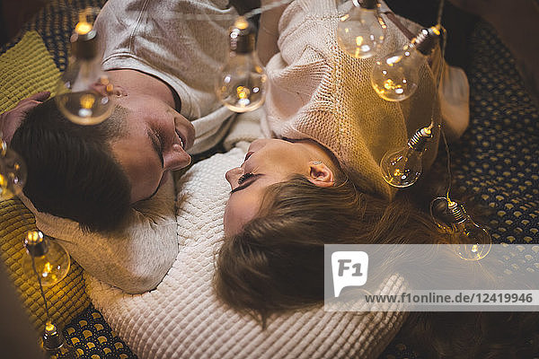 Romantic young couple cuddling in bed with fairy lights