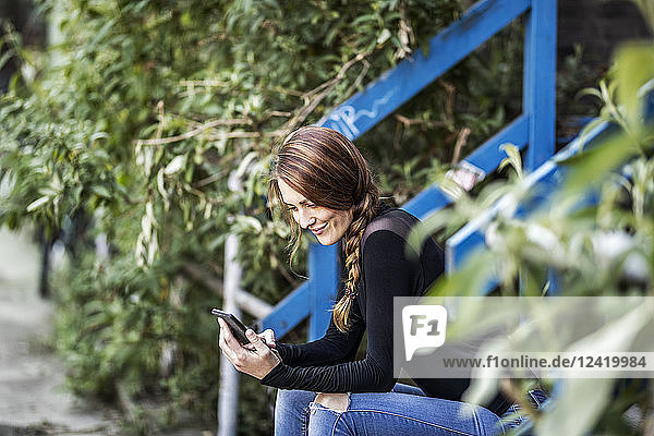 Smiling woman sitting on stairs looking at smartphone