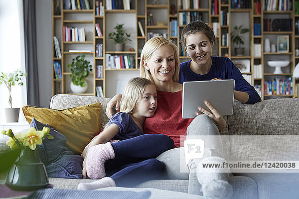 Mother and her daughters sitting on couch  having fun using digital laptop