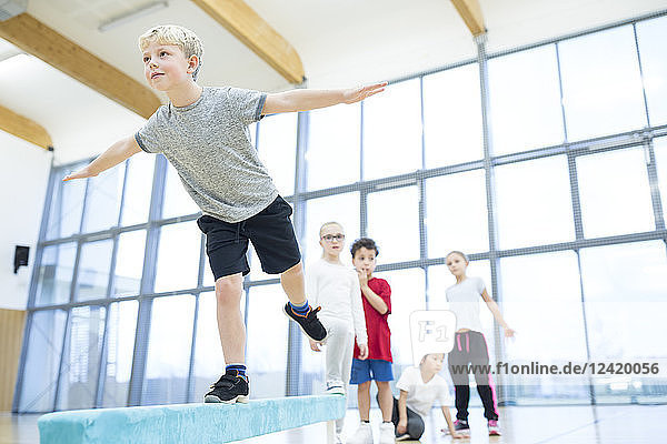 Schoolboy balancing on balance beam in gym class