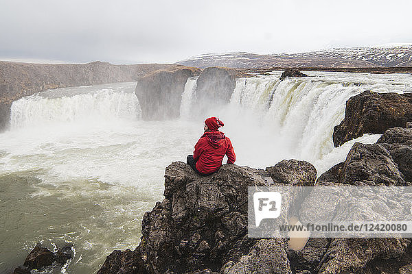 Iceland  man sitting at Godafoss waterfall