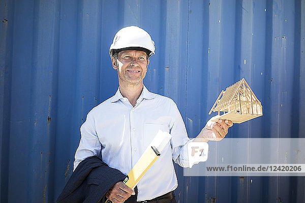Smiling architect wearing hard hat holding house model