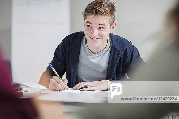 Smiling teenage boy taking notes in class