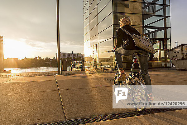 Senior woman with city bike at the riverside at sunset