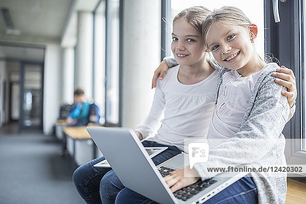 Portrait of two smiling schoolgirls with laptop and tablet embracing