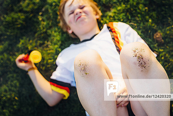 Boy in German soccer shirt lying on grass  with dirty knees